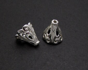 May include: Two silver filigree cone shaped bead caps. The caps have a decorative, openwork design.