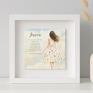 May include: A framed print with a watercolour illustration of a woman in a floral dress. The print includes the name "Jessica" and a poem. The frame is white, and the background is a light blue and white.