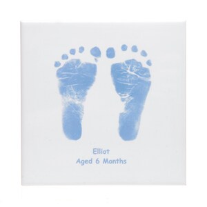 May include: A white canvas with two blue baby footprints, the text "Elliot Aged 6 Months" is printed below the footprints.