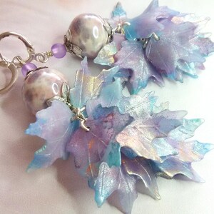 May include: A pair of earrings with iridescent purple and blue leaves dangling from a silver hoop and a white and pink marble bead.