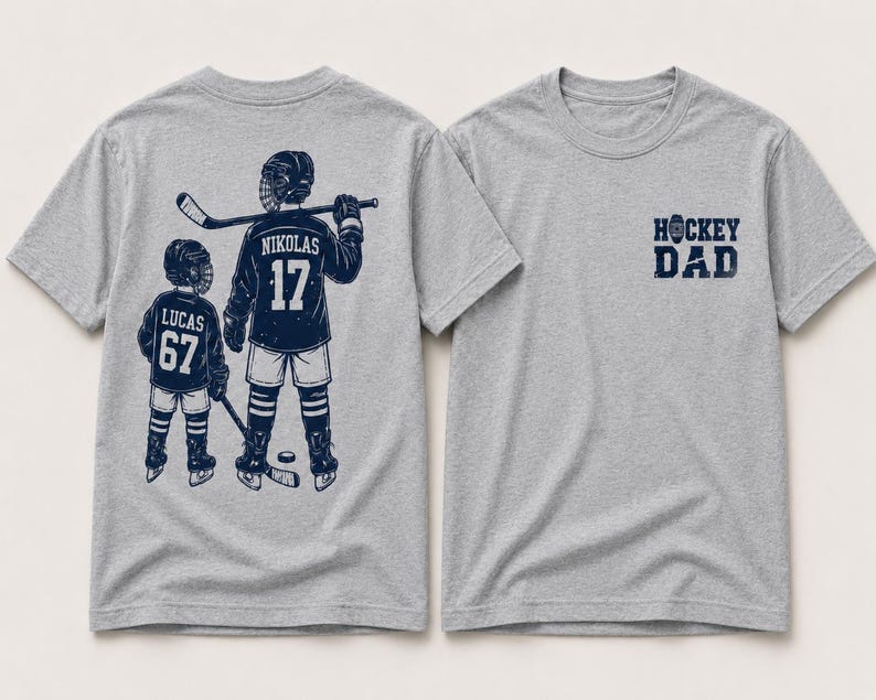 May include: Two gray t-shirts. One features a navy blue graphic of two hockey players with the names "Nikolas" and "Lucas" and the numbers 17 and 67. The other shirt has the text "HOCKEY DAD" in navy blue.