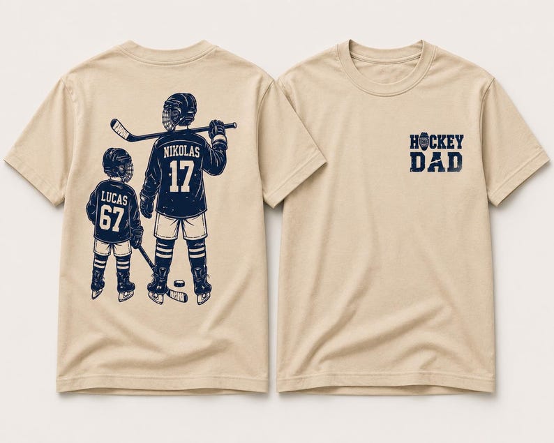 May include: Beige t-shirts with hockey-themed graphics. One shirt features a design of two hockey players with the text "NIKOLAS 17" and "LUCAS 67". The other shirt has the text "HOCKEY DAD" in navy blue.