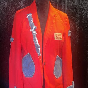 May include: A bright red blazer with denim patches and accents. The jacket features a Levi's label and denim detailing on the sleeves and pockets. The blazer is displayed on a black mannequin.