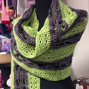 May include: A green and gray crocheted scarf with a lacy pattern. The scarf is draped over a mannequin.