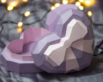 May include: A purple origami heart-shaped box with a white bow. The box is open and the inside is a lighter shade of purple.