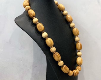 May include: A necklace featuring alternating large oval and small round wooden beads. The beads display a natural light brown wood grain pattern with darker brown swirls. The necklace is strung with small dark brown spacer beads between each wooden bead.