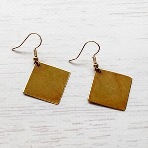 May include: A pair of gold square earrings with a simple design. The earrings have a hook closure.