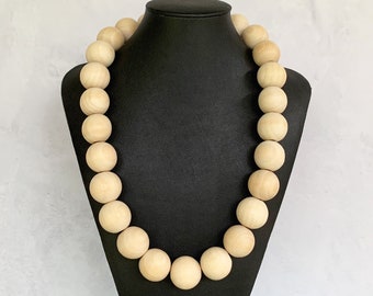 May include: A long necklace made of natural wood beads. The beads are round and have a smooth, polished finish. The necklace is displayed on a black mannequin.