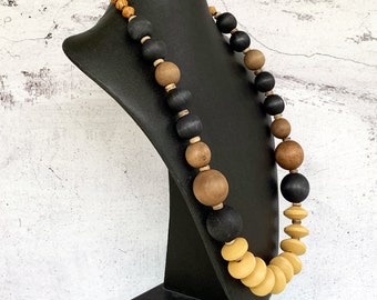 May include: A long necklace made of wooden beads in black, brown, and light brown colors. The necklace is displayed on a black mannequin.