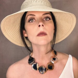May include: A statement necklace featuring large, polished, circular agate stones in shades of black, cream, and translucent amber. The stones are strung together on a dark cord, creating a bold, multi-colored accessory worn around the neck.