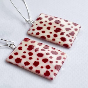 May include: A pair of earrings with a rectangular red and white shell design. The earrings are made with silver hooks.