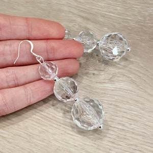 May include: A pair of long silver dangle earrings with three clear faceted crystal beads.