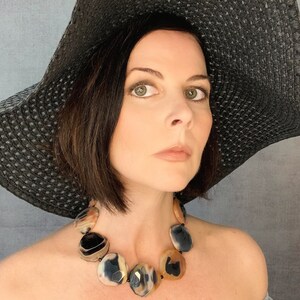 May include: A statement necklace featuring large, polished, faceted agate stones in shades of translucent amber, cream, and deep black. The stones are strung together with small black beads, creating a bold, multi-colored accessory that rests against the collarbone.