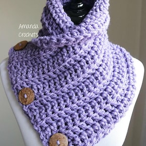 Puede incluir: Un cuello de punto de ganchillo morado con tres botones de madera. El cuello se muestra en un maniquí blanco.