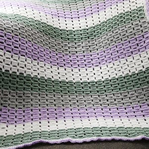 May include: A crocheted blanket with stripes of white, lavender, and green yarn. The blanket has a scalloped edge.