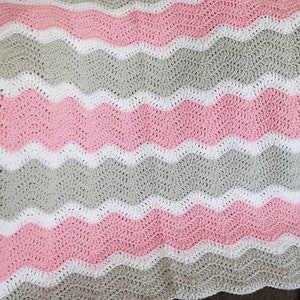 May include: A crocheted baby blanket with a wavy pattern in pink, white and grey.