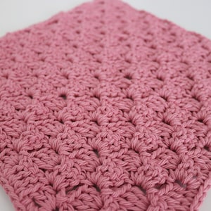 Puede incluir: Primer plano de un cuadrado de crochet rosa. El cuadrado está hecho con un patrón de punto simple y tiene un aspecto suave y texturizado.