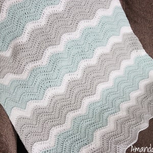May include: A crocheted baby blanket with a chevron pattern in shades of white, grey, and light blue.