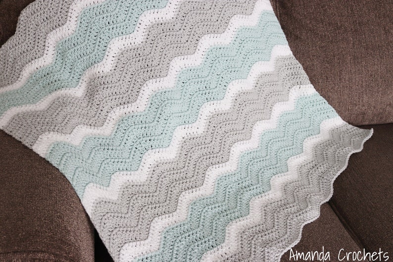 May include: A crocheted baby blanket with a chevron pattern in shades of white, grey, and light blue.
