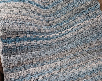 Pode incluir: Uma manta de crochê em um esquema de cores azul e cinza. A manta é feita com um ponto texturizado que cria um visual tecido.