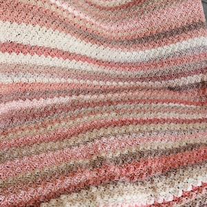 K&ouml;nnte beinhalten: Eine geh&auml;kelte Decke mit einem gestreiften Muster in Rosat&ouml;nen, Braun und Beige. Die Decke ist mit einem strukturierten Stich gearbeitet, der eine erhabene, unebene Oberfl&auml;che erzeugt.