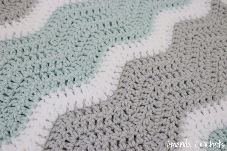 May include: A crocheted baby blanket with a chevron pattern in shades of grey, white, and light blue.