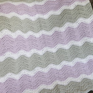 May include: A crocheted baby blanket with a wavy pattern in shades of lavender, white, and grey.