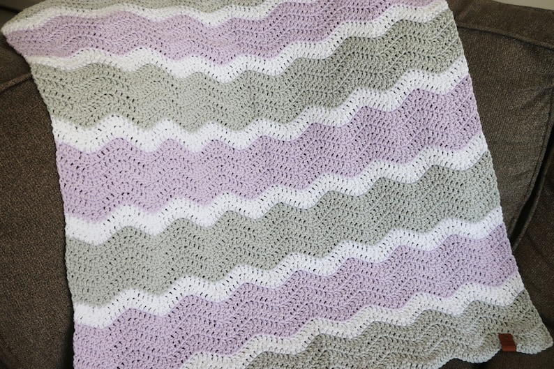 May include: A crocheted baby blanket with a wavy pattern in shades of lavender, white, and grey.