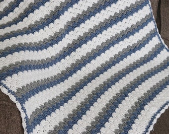 May include: A crocheted baby blanket with a chevron pattern in white, gray, and blue.