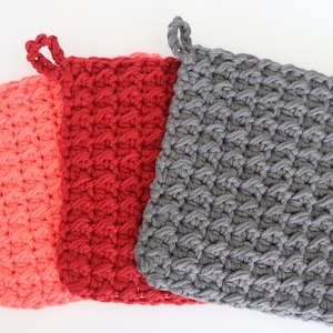 May include: Three crocheted pot holders in coral, red, and grey. The pot holders are square with a loop handle at the top.