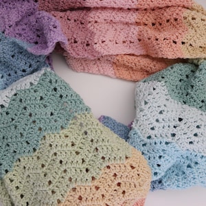 May include: A rainbow crochet scarf with a chevron pattern. The scarf is made of soft yarn and has a light and airy feel.