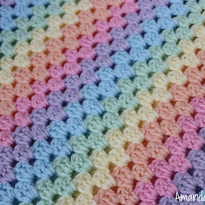 Op de afbeelding: Een regenboog gehaakte deken met een verloop van pastelkleuren, waaronder paars, blauw, groen, geel, oranje en roze.