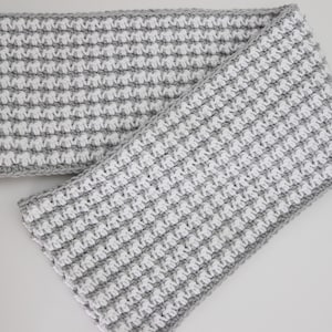 May include: A grey and white crocheted infinity scarf with a textured pattern.