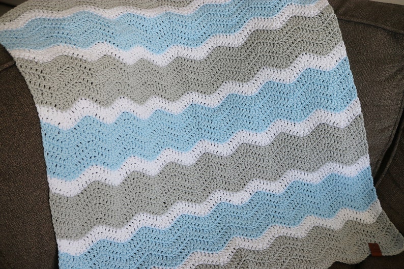 May include: A crocheted baby blanket with a wavy pattern in shades of blue, grey, and white.