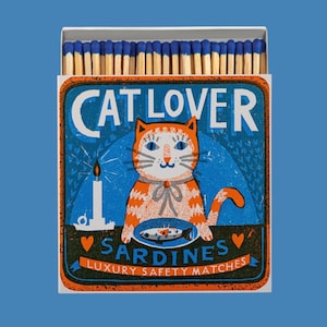 May include: A matchbox with a blue and orange design featuring a cartoon cat with the text "CAT LOVER" above it. The box also includes the text "SARDINES LUXURY SAFETY MATCHES". The matches have blue tips.