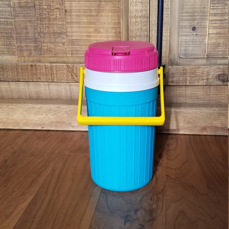 May include: A blue and white cooler with a pink lid and a yellow handle. The cooler is made of plastic and has a ribbed design.
