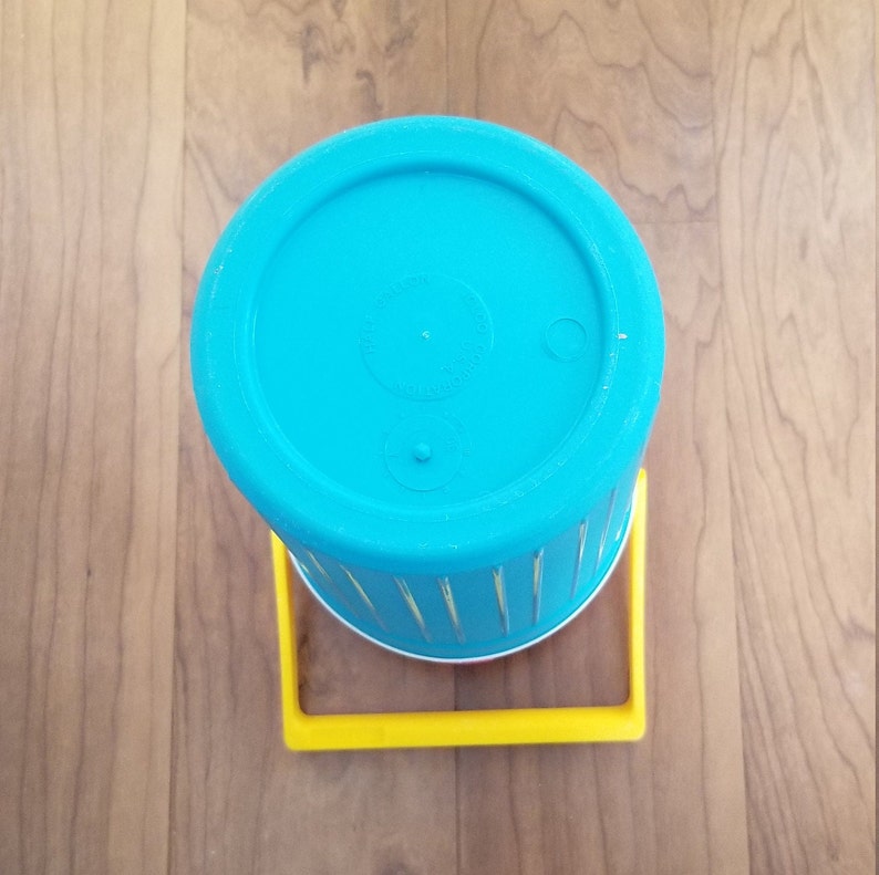 May include: A blue plastic cup with a yellow plastic handle. The cup has a white stripe around the top and a white stripe around the bottom.