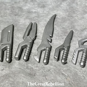 May include: A set of six silver-colored plastic toy weapons. The weapons are all different shapes and sizes, and they have a futuristic design.