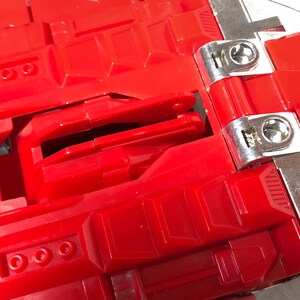 Puede incluir: Juguete de pl&aacute;stico rojo con una bisagra plateada y un pestillo plateado. El juguete tiene un dise&ntilde;o detallado con m&uacute;ltiples compartimentos y una superficie texturizada.