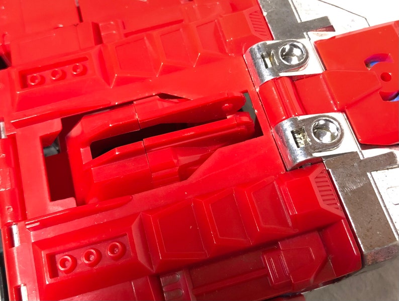 Puede incluir: Juguete de pl&aacute;stico rojo con una bisagra plateada y un pestillo plateado. El juguete tiene un dise&ntilde;o detallado con m&uacute;ltiples compartimentos y una superficie texturizada.