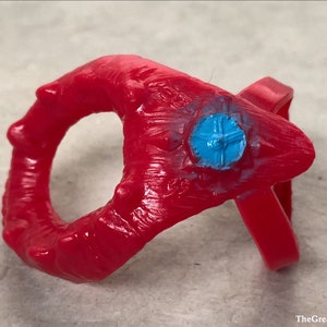 May include: A red plastic ring with a blue plastic centre piece. The ring has a textured surface and is decorated with small spikes.