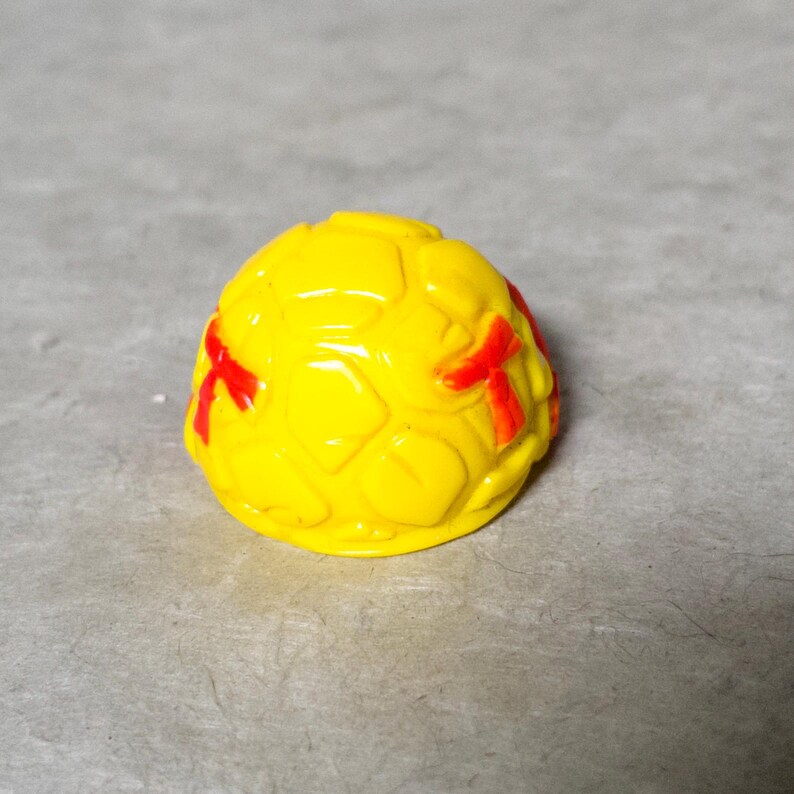 K&ouml;nnte beinhalten: Gelbe Plastik-Schildkr&ouml;tenschale mit roten Markierungen. Die Schale hat eine strukturierte Oberfl&auml;che und ist in Form einer Schildkr&ouml;tenschale.