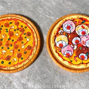 Peut inclure: Deux tranches de pizza jouet avec des garnitures différentes. Une tranche a du pepperoni, des champignons et des poivrons verts. L'autre tranche a des champignons, du pepperoni et des garnitures roses et blanches qui ressemblent à des cerises.