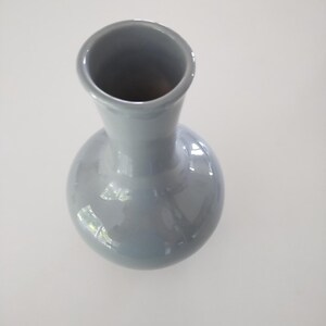 May include: A gray ceramic vase with a rounded body and a narrow neck. The vase has a glossy finish and reflects light. The vase is a decorative item.