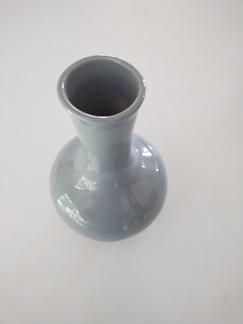 May include: A gray ceramic vase with a rounded body and a narrow neck. The vase has a glossy finish and reflects light. The vase is a decorative item.