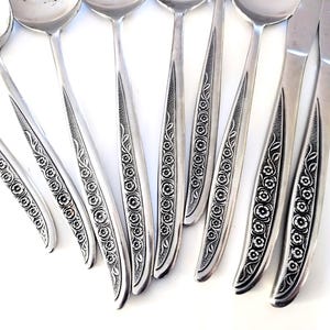 May include: A collection of vintage silverware, including spoons and knives, with a floral design etched into the handles. The silverware is made of a shiny, silver-colored metal and is arranged on a white surface.