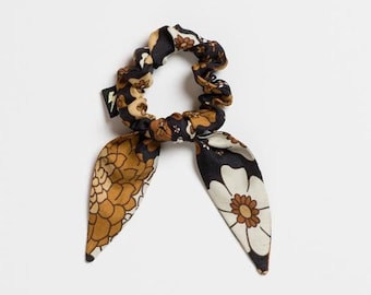 May include: A black and brown floral patterned hair scrunchie with two long tails.
