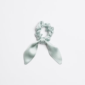 Könnte beinhalten: Ein hellblauer Satin-Haargummi mit zwei langen Bändern. Der Haargummi ist zu einem Knoten gebunden und die Bänder hängen herunter.