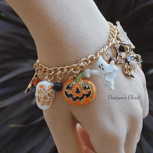 May include: Gold-toned charm bracelet with Halloween-themed charms. Charms include a jack-o'-lantern, skull, ghost, and spider. The bracelet is worn on a wrist. The text "Destyny's Closet" is visible.