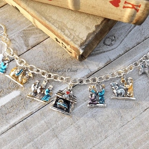 May include: A silver charm bracelet featuring religious-themed charms. The charms depict scenes from the Nativity story, including the Three Wise Men, the Holy Family, and the manger. The bracelet is displayed on a rustic wooden surface.